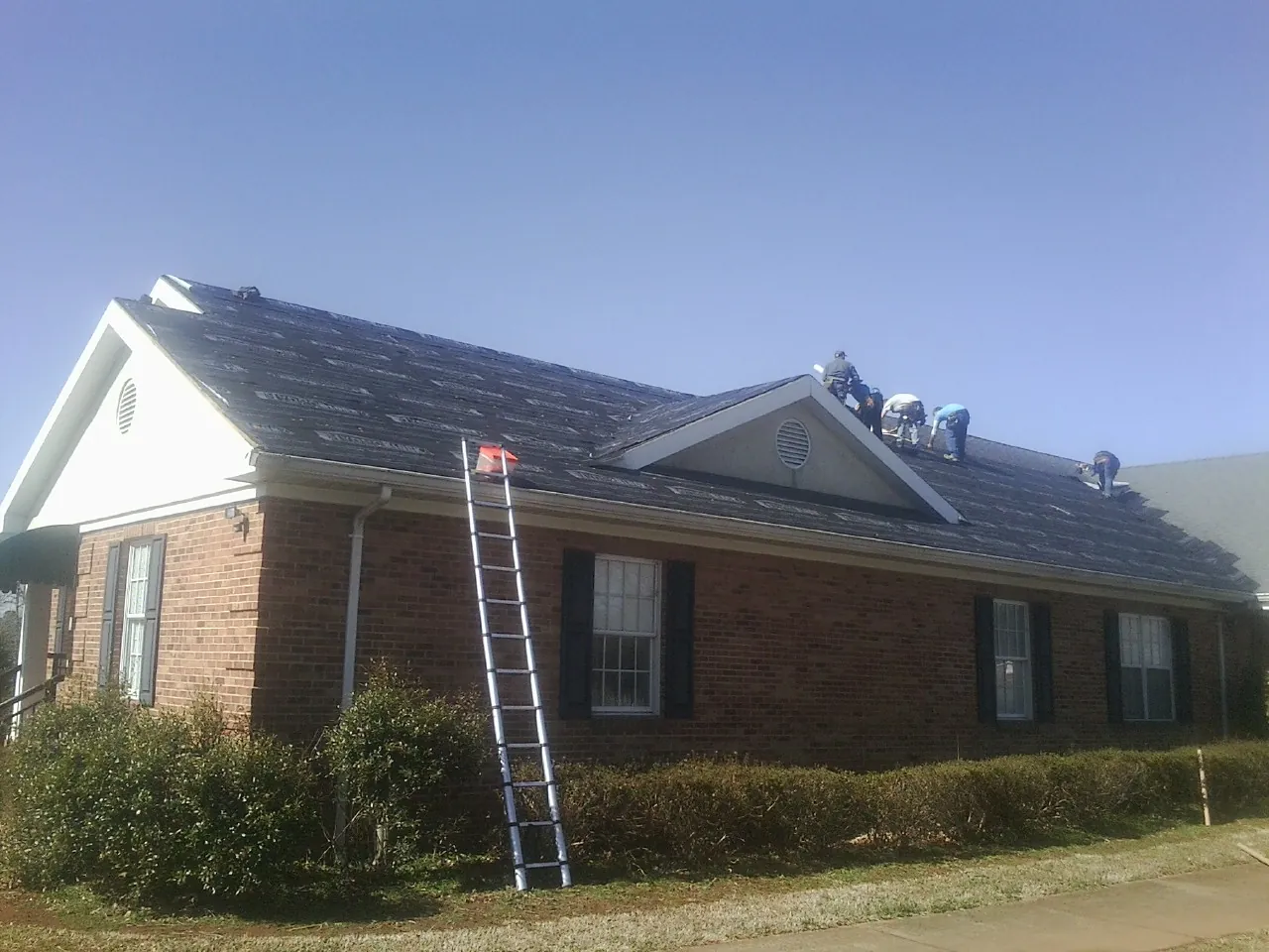 Crew tearing shingles off a brick ranch roof with a ladder set — Metal Roof Repair work by our crew in Lancaster